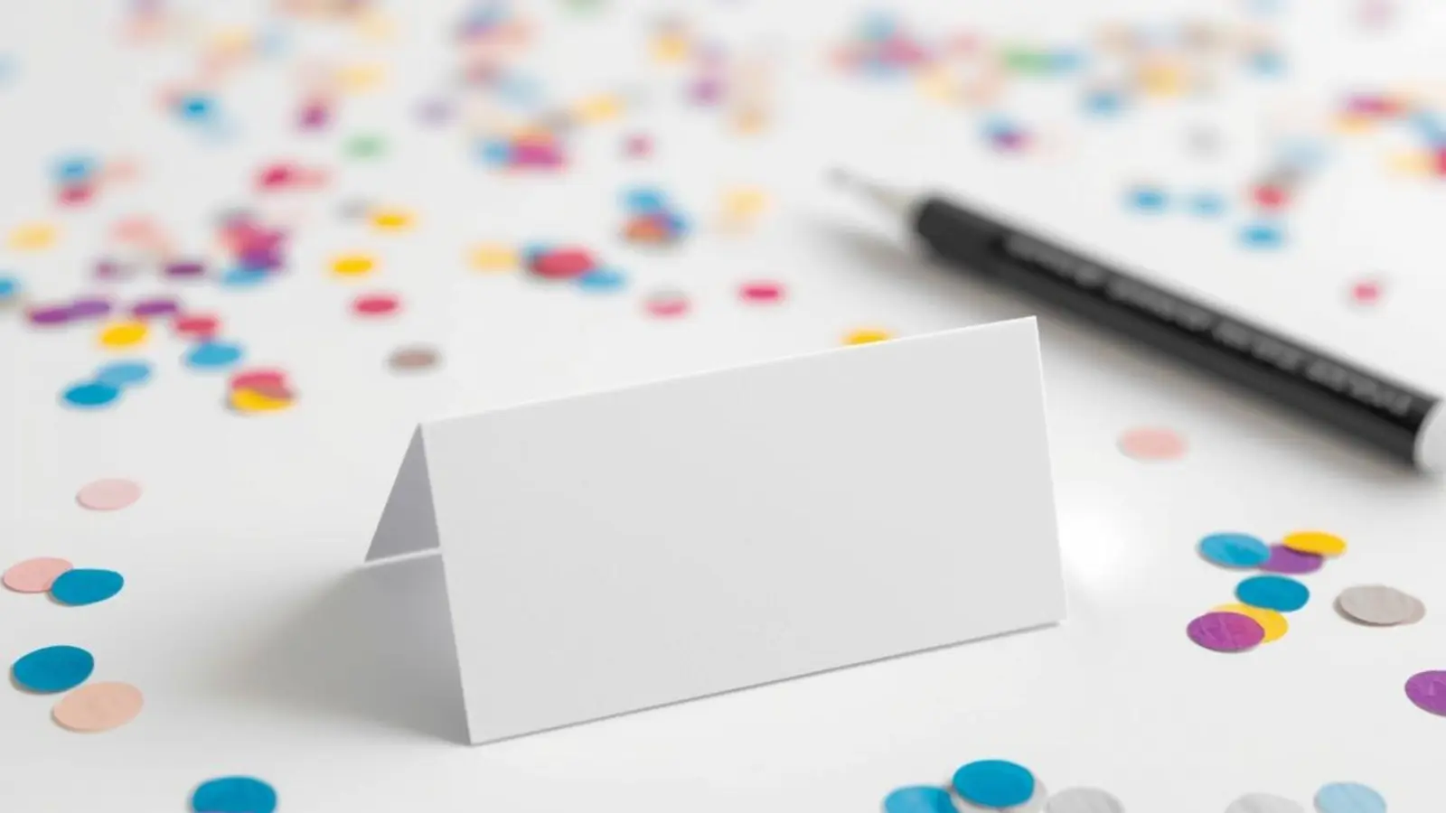 Blank name tag and marker on a clean desk with soft confetti blur.